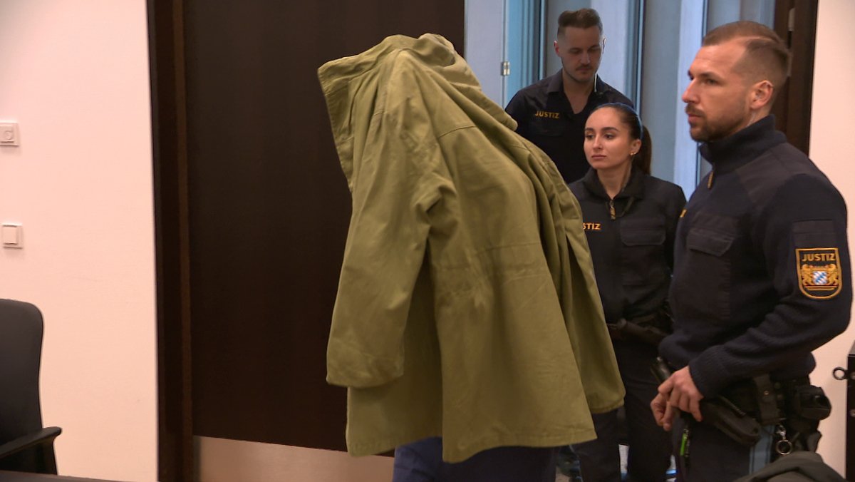 Ein Angeklagter läuft mit Jacke über den Kopf durch den Gerichtssaal.