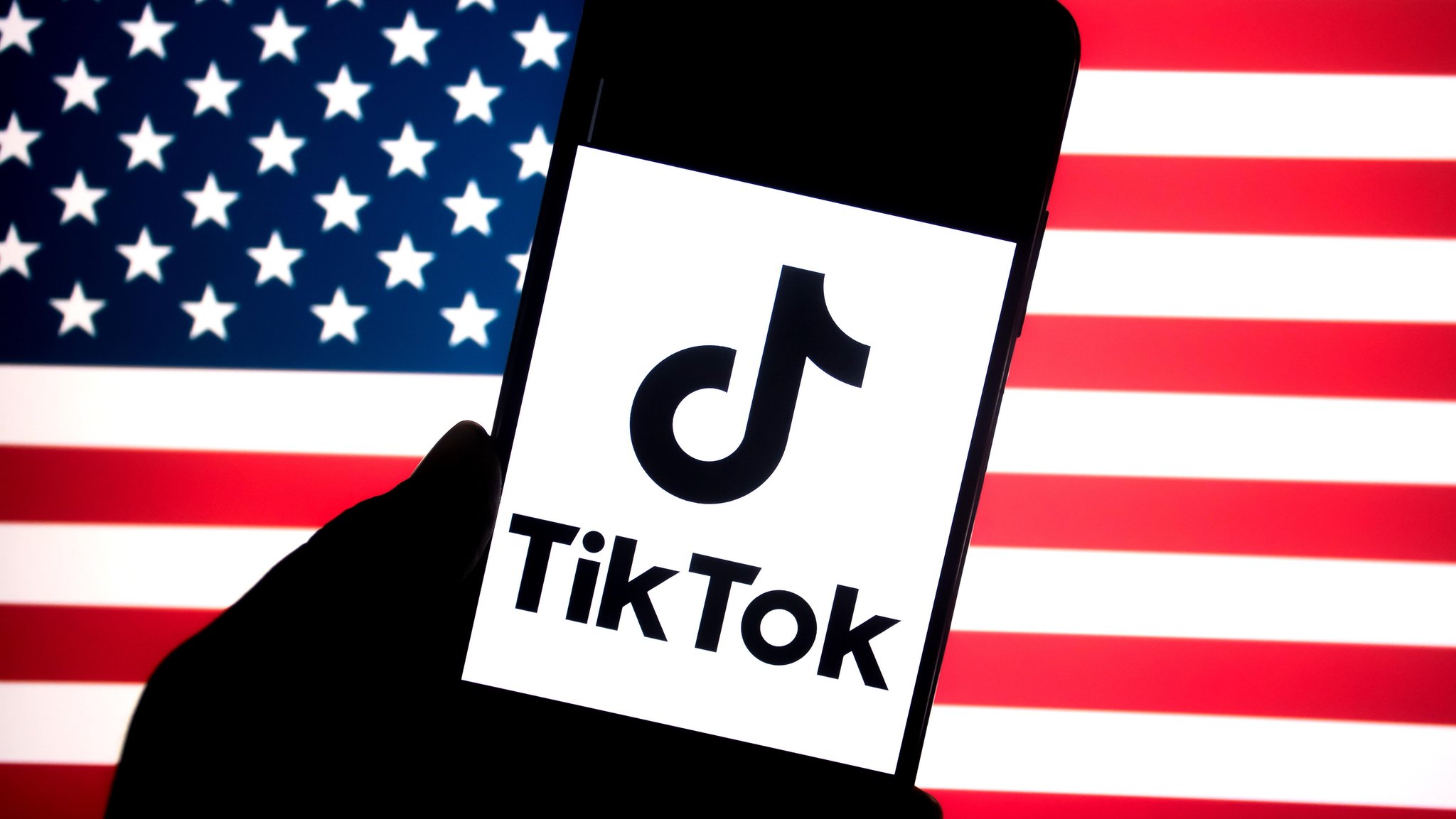 Symbolbild: Ein angedeutetes Smartphone mit TikTok-Schriftzug vor US-Flagge