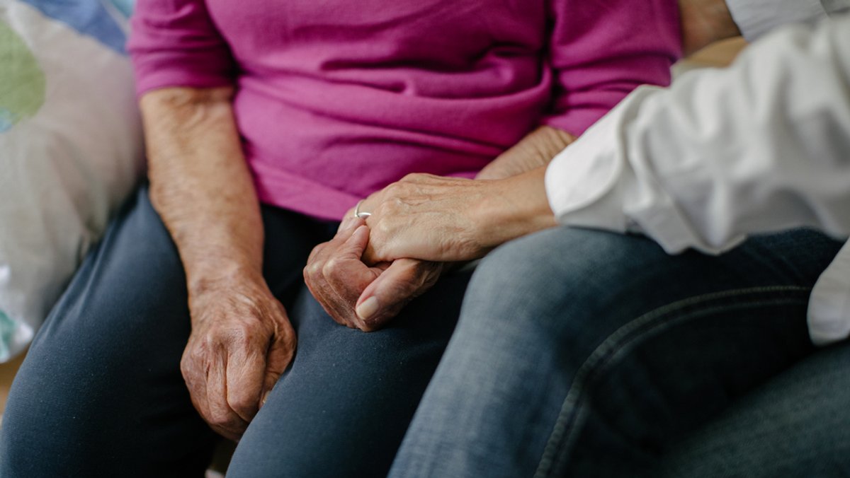 Eine Pflegerin hält die Hände einer Seniorin.