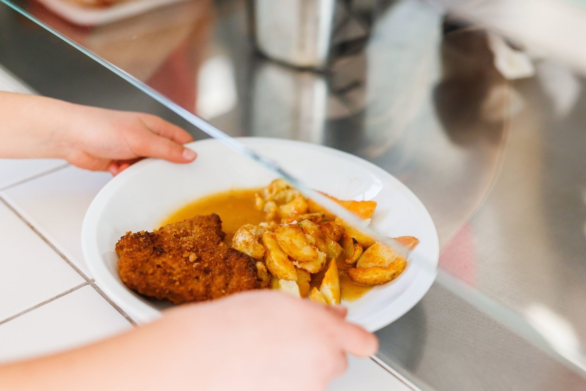 18.10.2022, Baden-Württemberg, Freiburg: Eine Grundschülerin nimmt einen Teller mit Schnitzel, Kartoffeln und Sauce vom Tresen der Essensausgabe einer Schulmensa. Ab dem Schuljahr 2023/2024 soll in Grundschulen und Kitas nur noch ein Gericht angeboten werden, das vegetarisch ist. 