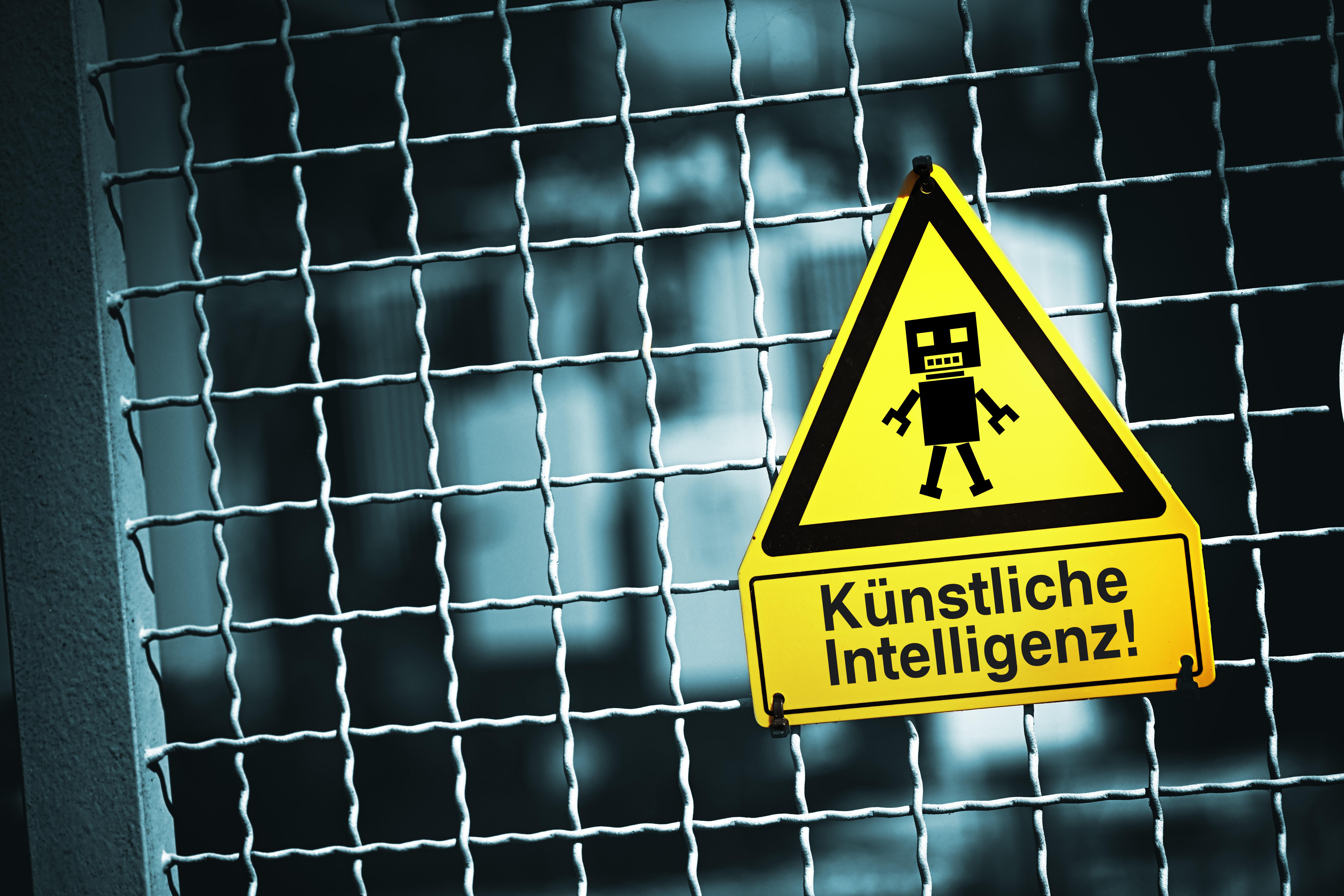 Symbolbild: Roboterfigur auf einem Warnschild mit Aufschrift Künstliche Intelligenz