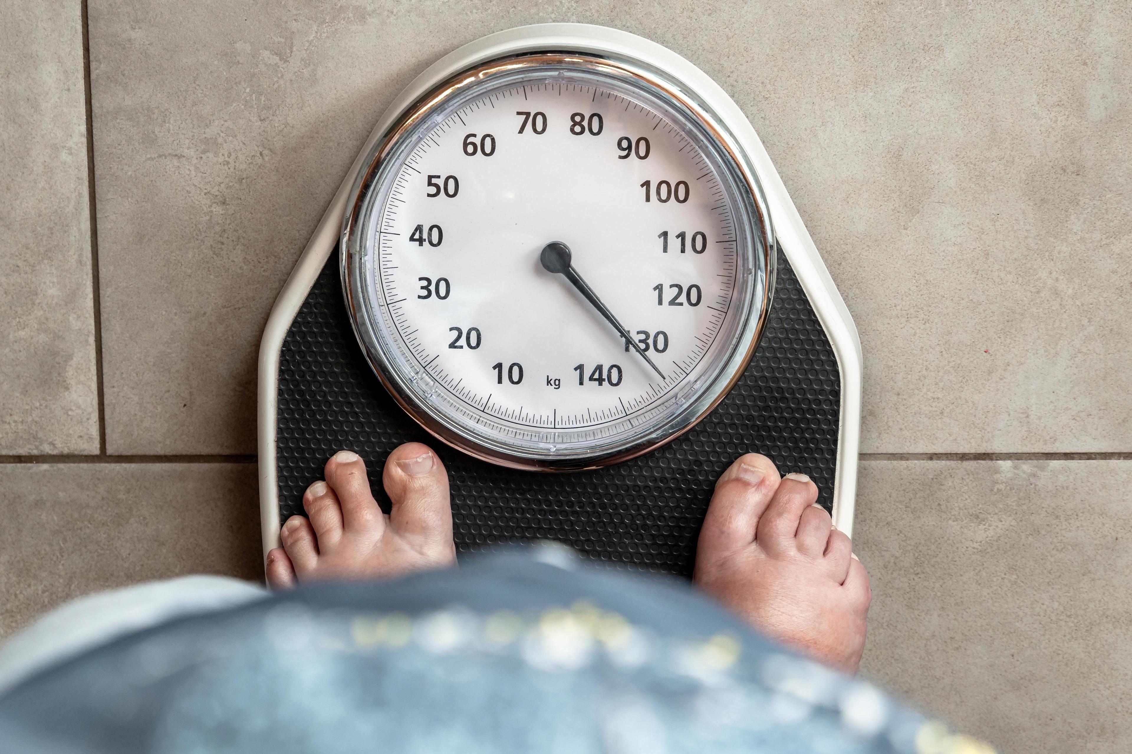 Symbolbild: Eine Person steht barfuß auf einer Waage, die mehr als 130 Kilogramm anzeigt.Gesundheit und Übergewicht
