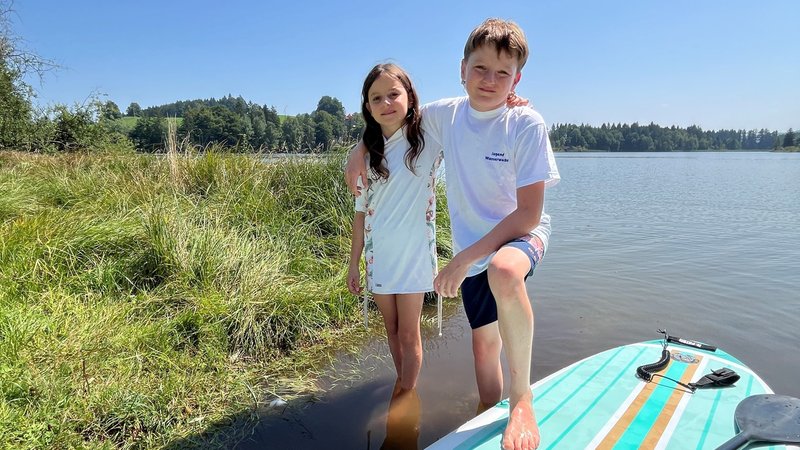 Ein Junge und ein Mädchen am Rand eines Weihers. Der Junge hat einen Fuß auf einem Stand Up Paddle-Board. | Bild: BR/Thomas Pösl Ein Junge und ein Mädchen am Rand eines Weihers. Der Junge hat einen Fuß auf einem Stand Up Paddle-Board.