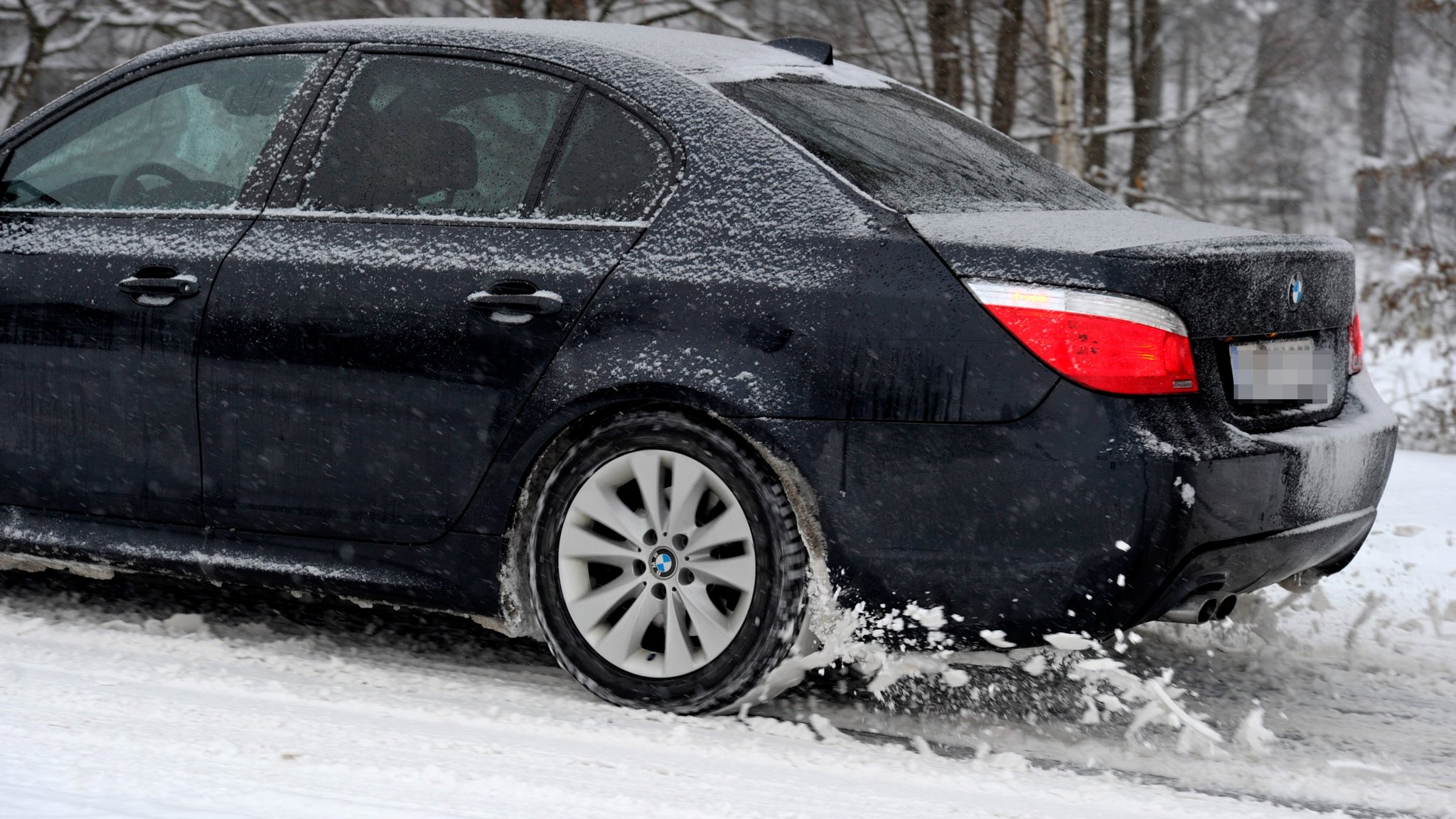 Winter im Allgäu, Winterreifen - Der Reifen eines BMW dreht auf der schneebedeckten Strasse durch.