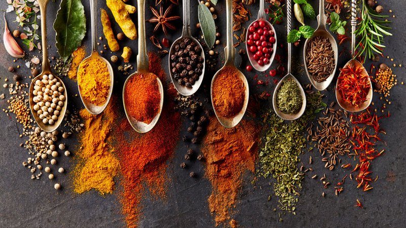 Gewürze und Kräuter aus aller Welt auf verschiedene Löffel gehäuft und auf dunkelgrauem Untergrund ausgestreut. | Bild: stock.adobe.com/Dionisvera Gewürze und Kräuter aus aller Welt auf verschiedene Löffel gehäuft und auf dunkelgrauem Untergrund ausgestreut.