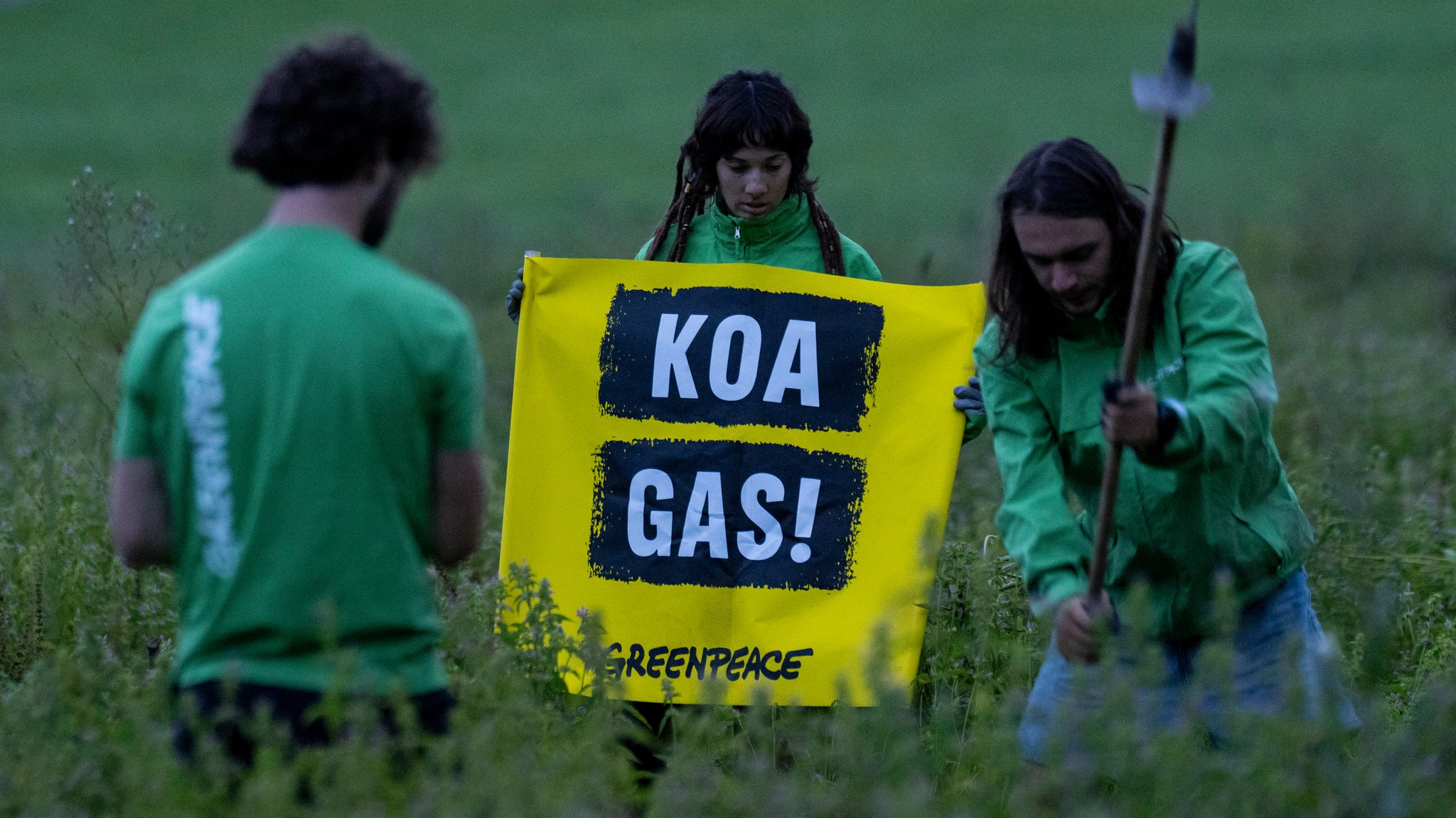 Drei Demonstranten der Umweltschutzorganisation Greenpeace in grünen T-Shirts demonstrieren gegen geplante Gasbohrung in Reichling - eine Frau hält ein gelbes Plakat mit der Aufschrift  "Koa Gas!"