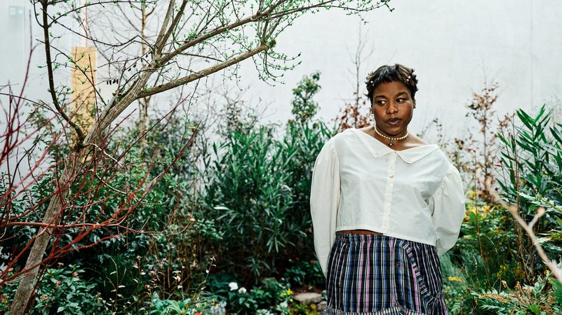 Precious Okoyomon steht in einem gestalteten Raum, das einem wilden Garten gleichkommt. | Bild: Miro Kuzmanovic © Kunsthaus Bregenz Precious Okoyomon steht in einem gestalteten Raum, das einem wilden Garten gleichkommt.