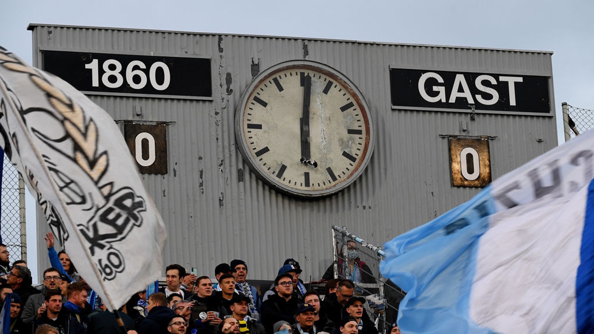 ARCHIV - 26.10.2021, Bayern, München: Fußball: DFB-Pokal, TSV 1860 München - FC Schalke 04, 2. Runde, Stadion an der Grünwalder Straße. Fahnen wehen vor der alten Spielstandanzeige. (zu dpa: «Ismaiks (unmoralisches) 100-Millionen-Angebot für die «Löwen»») Foto: Angelika Warmuth/dpa - WICHTIGER HINWEIS: Gemäß den Vorgaben der DFL Deutsche Fußball Liga bzw. des DFB Deutscher Fußball-Bund ist es untersagt, in dem Stadion und/oder vom Spiel angefertigte Fotoaufnahmen in Form von Sequenzbildern und/oder videoähnlichen Fotostrecken zu verwerten bzw. verwerten zu lassen. +++ dpa-Bildfunk +++