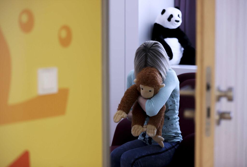 Ein Kind sitzt mit einem Kuscheltier im Arm (gestellte Szene)