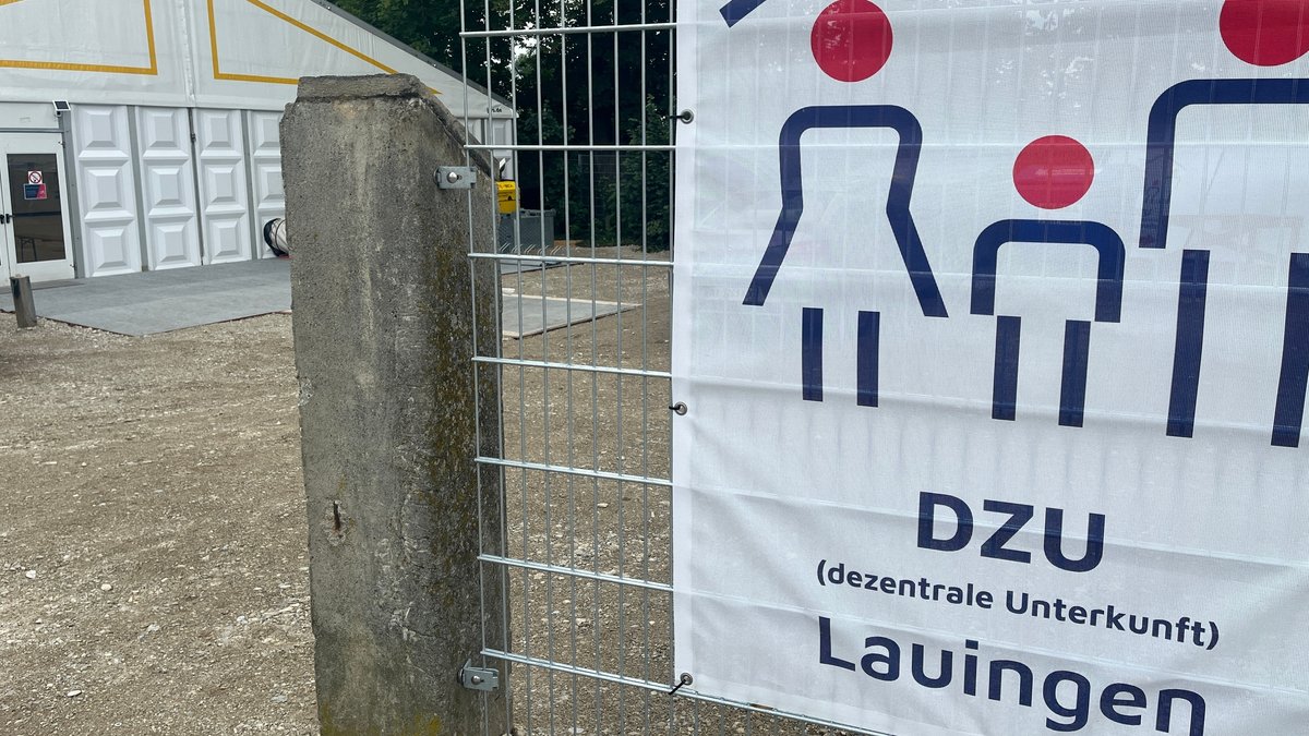 Das Flüchtlingszelt steht aktuell in Lauingen. An einem Zaun vor dem Zelt hängt ein Plakat, auf dem steht: DZU dezentrale Unterkunft 