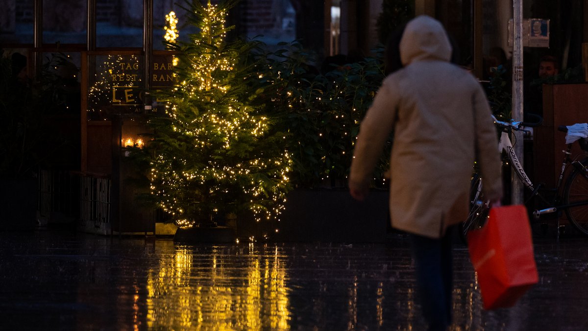 Ein Mann geht mit seinen Einkäufen in München an einem Weihnachtsbaum in der Fußgängerzone vorbei. 