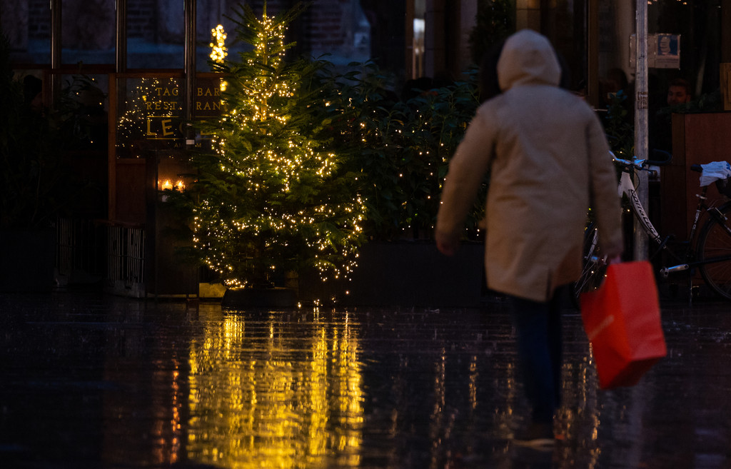 Ein Mann geht mit seinen Einkäufen in München an einem Weihnachtsbaum in der Fußgängerzone vorbei. 