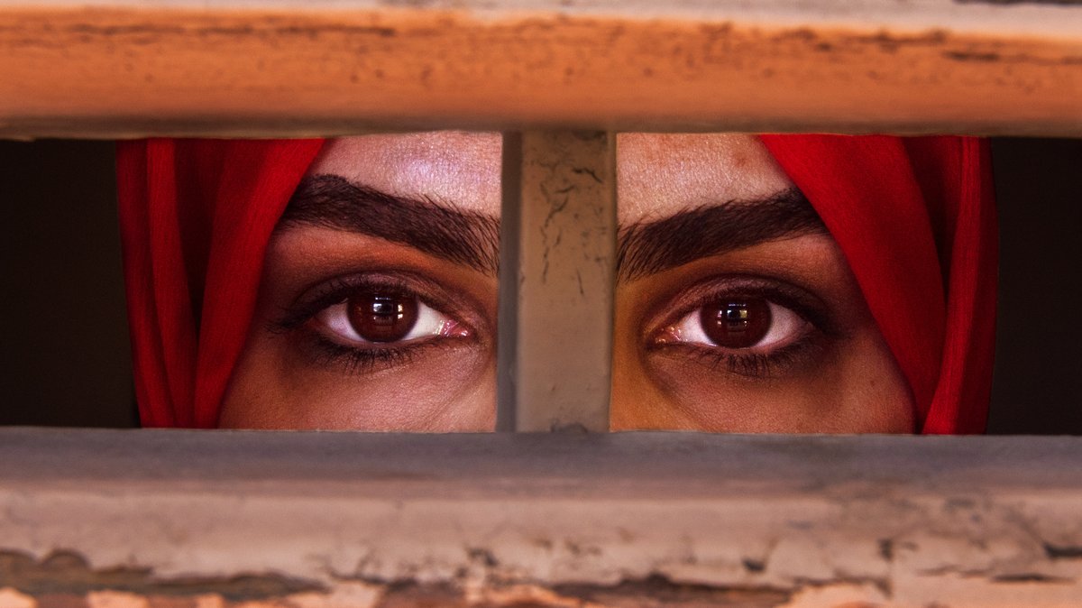 Liza Anvary, eine afghanische Geflüchtete steht hinter einem Holzfenster, als befände sie sich im Gefängnis - um, die Situation der Frauen in ihrem Land darzustellen.