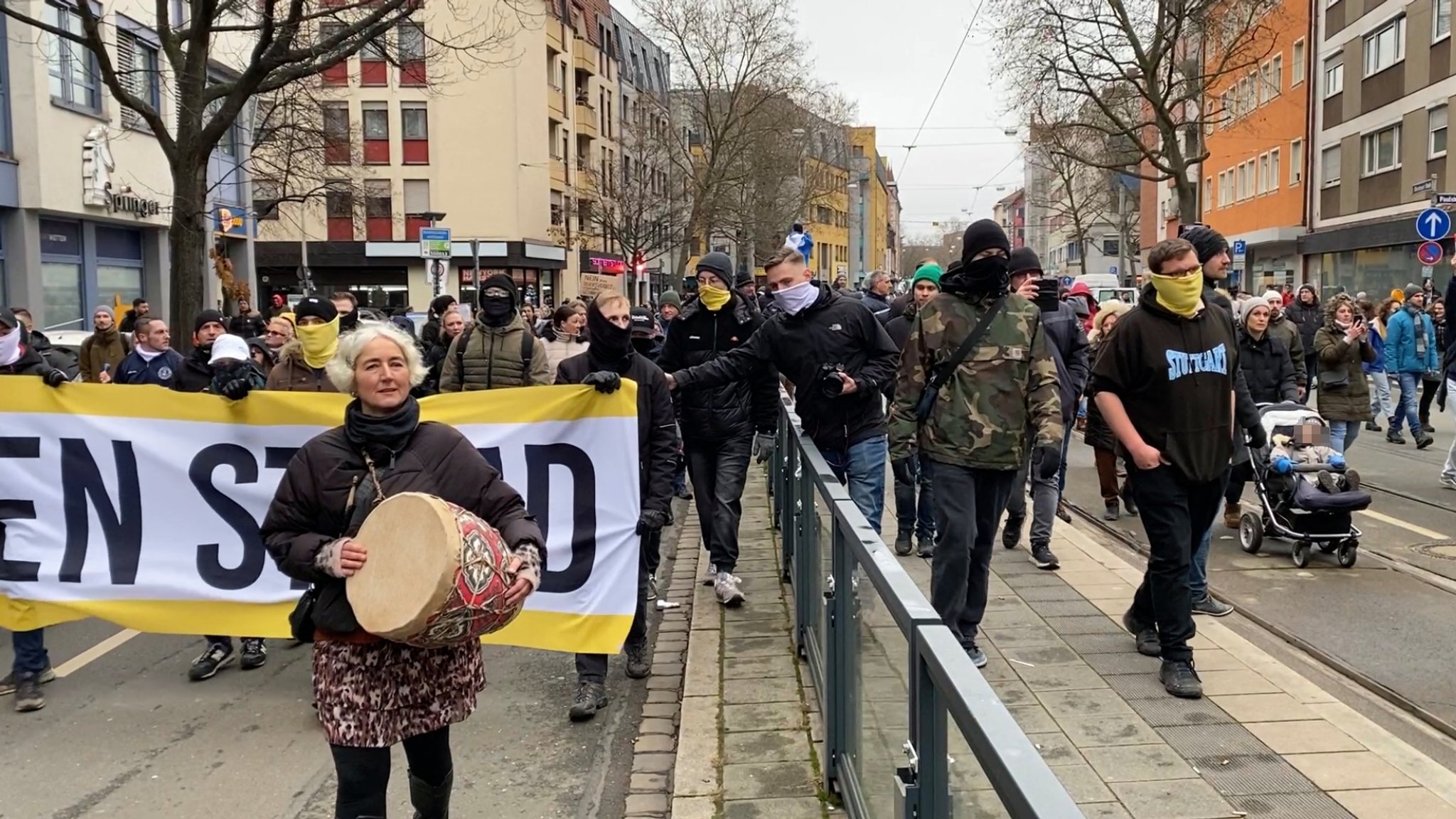 Eine Trommlerin läuft vor vermummten Anhängern einer rechten Gruppierung. 