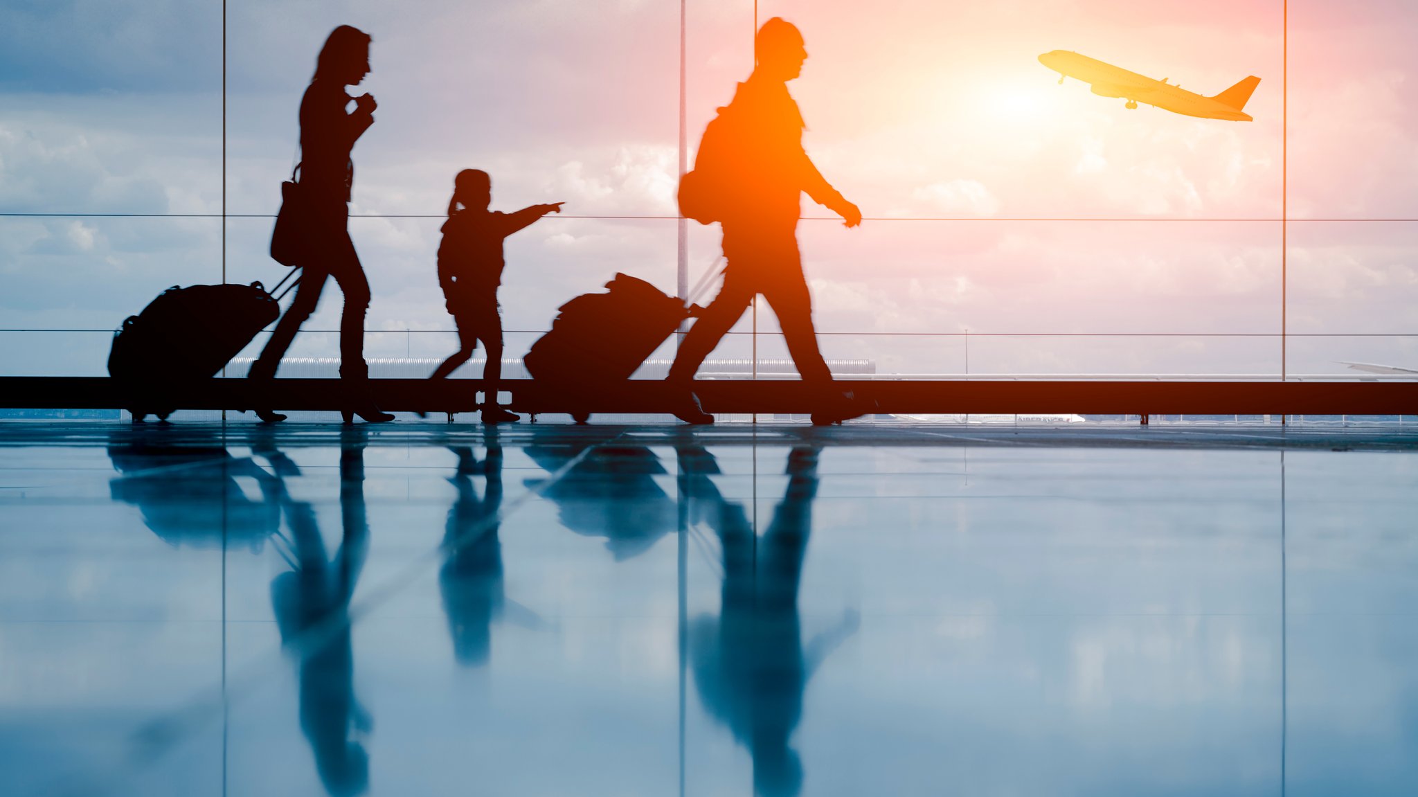 Silhouette einer jungen Familie mit Koffern, im Hintergrund ein startendes Flugzeug