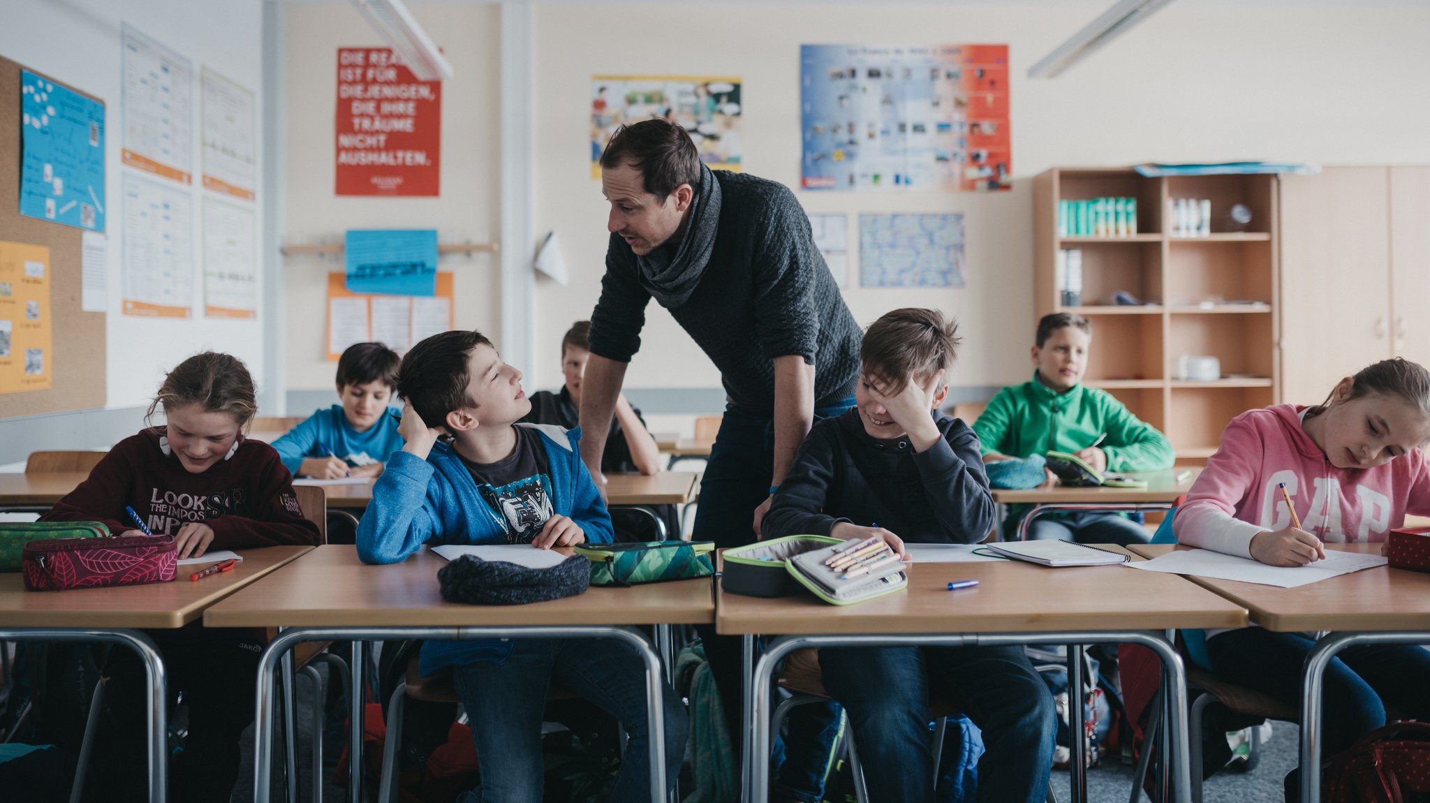 Lehrer steht im Klassenzimmer zwischen Schülerinnen und Schülern. | Bild: BR/Julia Müller Lehrer steht im Klassenzimmer zwischen Schülerinnen und Schülern.