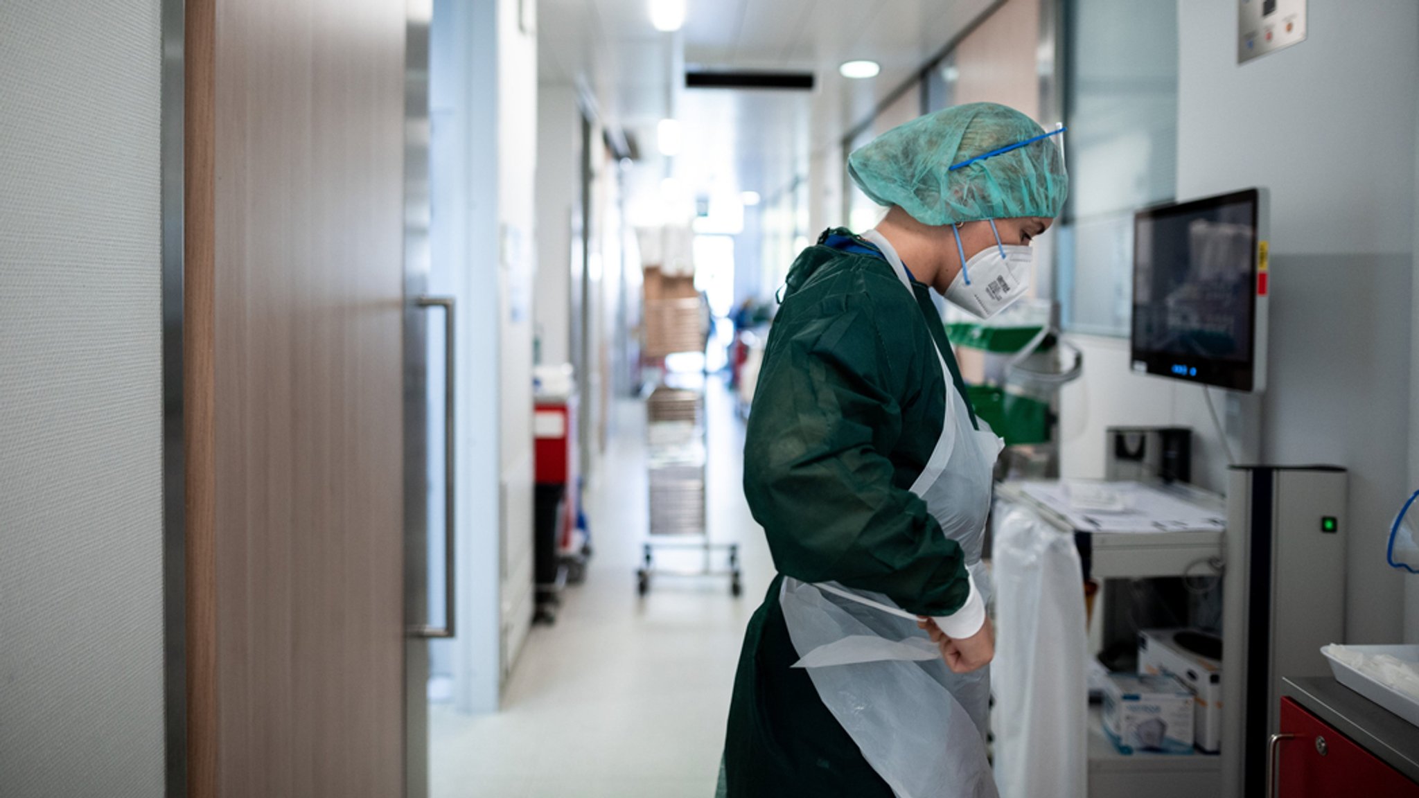 Eine Pflegerin, die Schutzkleidung trägt, steht auf einem Krankenhausflur.