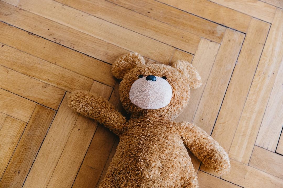 Ein Teddy-Bär liegt auf dem Holzboden.