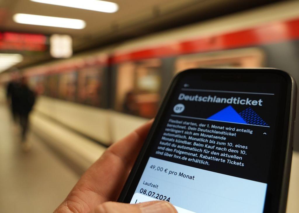 Ein Fahrgast hält ein Smartphone mit einem digitalen Deutschlandticket an einer U-Bahnstation in der Hand.