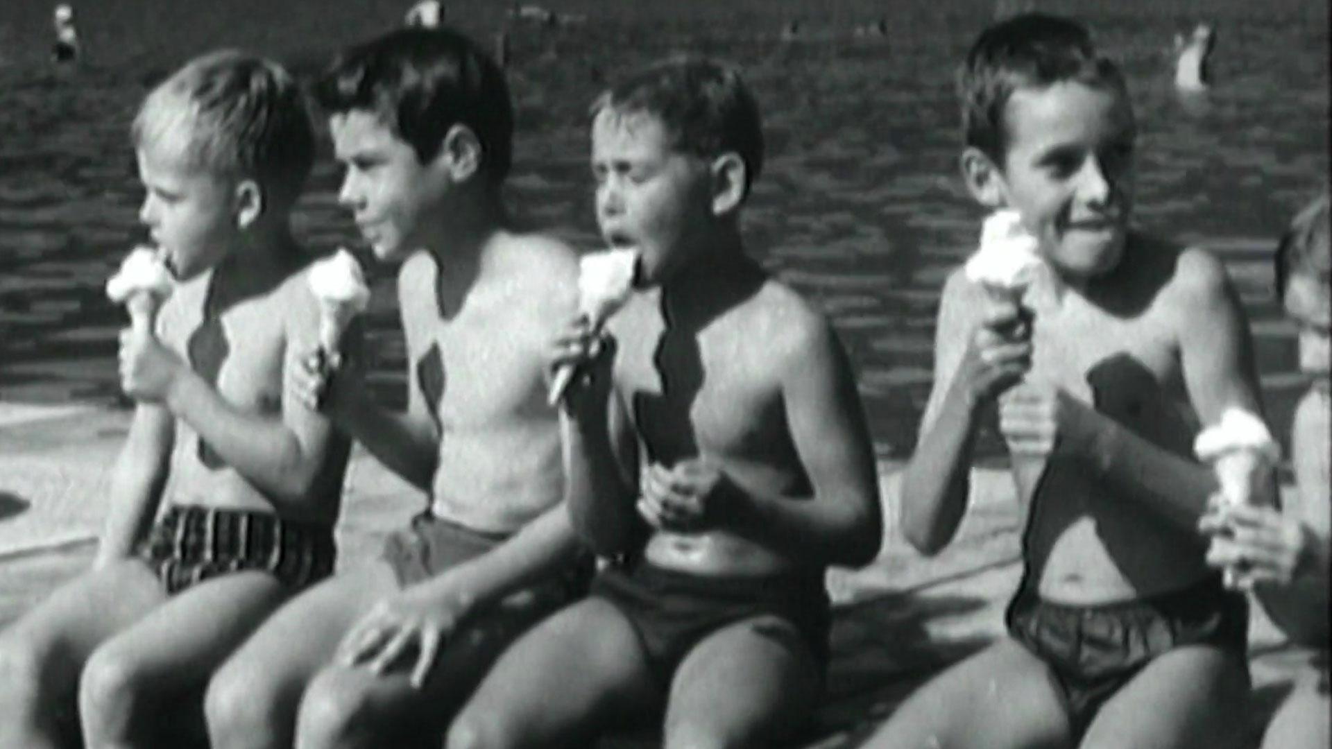 Kinder aus den fünfziger Jahren, die ein Eis essen und am Badesee sitzen