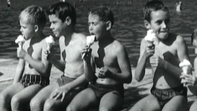 Kinder aus den fünfziger Jahren, die ein Eis essen und am Badesee sitzen