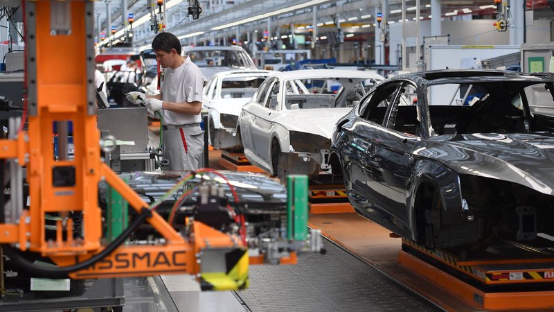 Ein Mitarbeiter eines Autoherstellers steht an einem Fließband. | Bild: picture alliance / Sven Simon Ein Mitarbeiter eines Autoherstellers steht an einem Fließband.