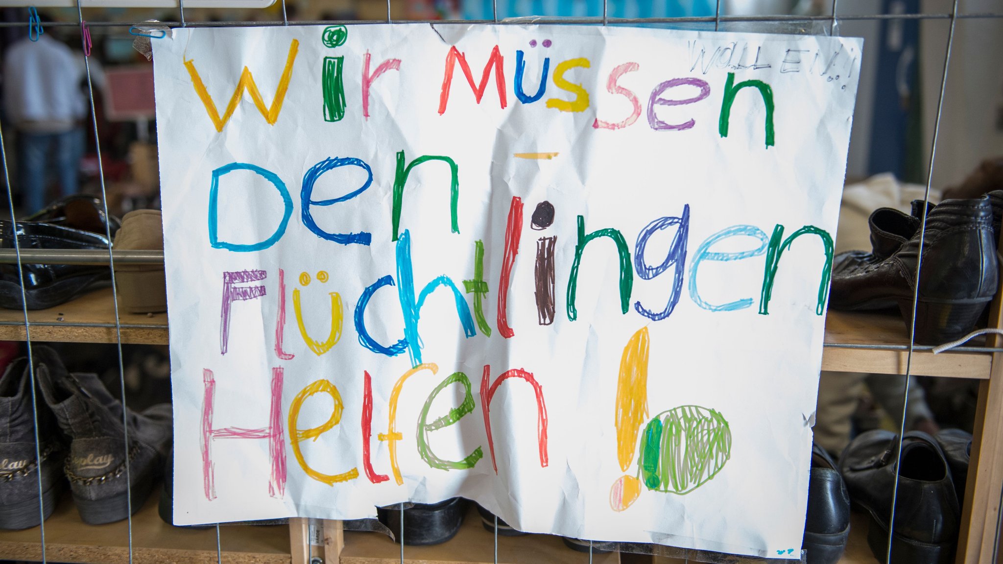 Ein buntes Plakat mit der Aufschrift: "Wir müssen den Flüchtlingen helfen!"