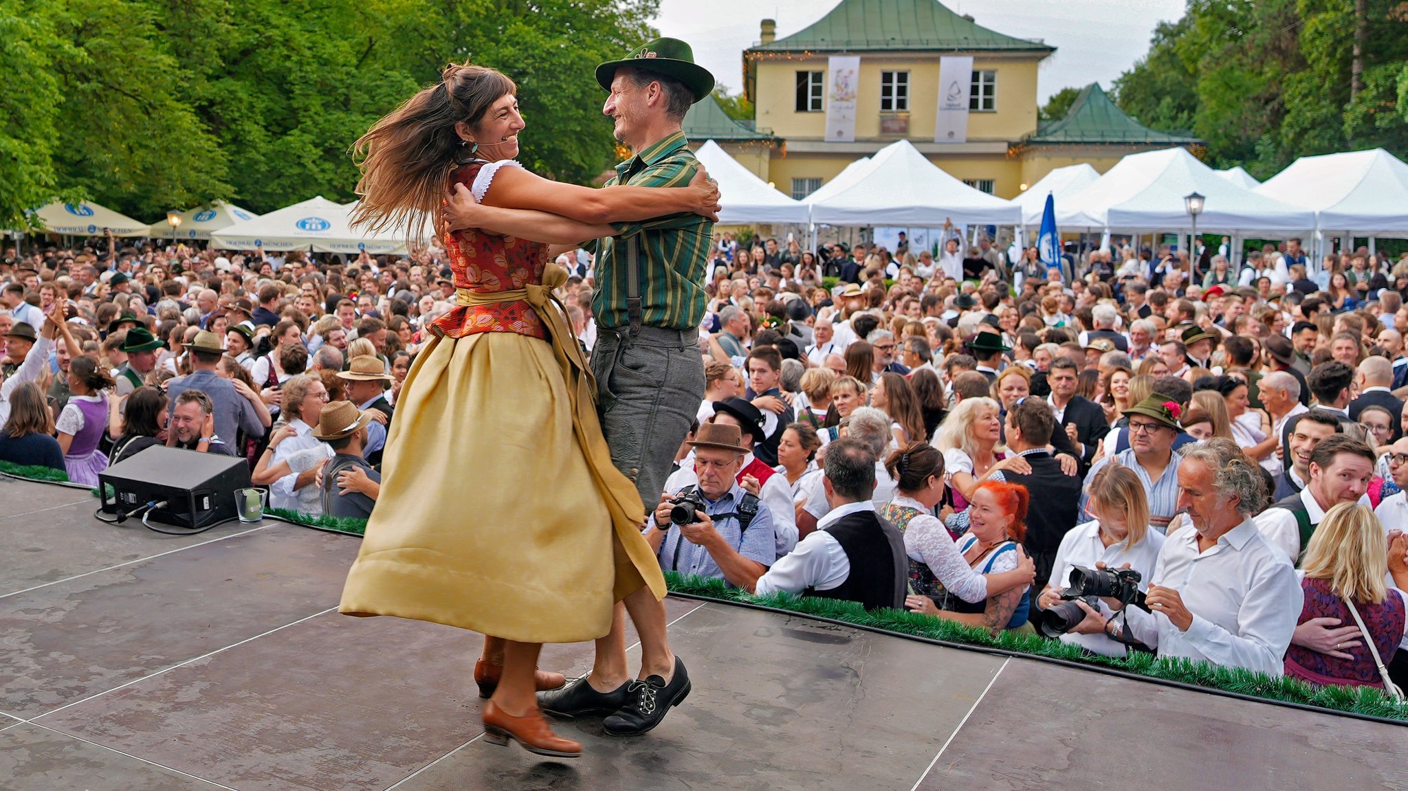 dpatopbilder - 19.07.2026, Bayern, München: Katharina Mayer und Magnus Kaindl zeigen als Tanzmeister von der Bühne herab beim Kocherlball am Chinesischen Turm die Tanzschritte. Das traditionelle Freiluft-Volkstanzfest bei Sonnenaufgang im Englischen Garten nahm seinen Anfang um das Jahr 1880. Es findet seit 1989 wieder statt, in der Regel am 3. Sonntag im Juli. Foto: Uwe Lein/dpa +++ dpa-Bildfunk +++
