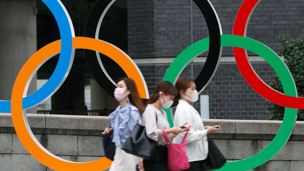 Japan, Tokio: Menschen mit Gesichtsmasken gehen an der Statue der Olympischen Ringe in Tokio vorbei.