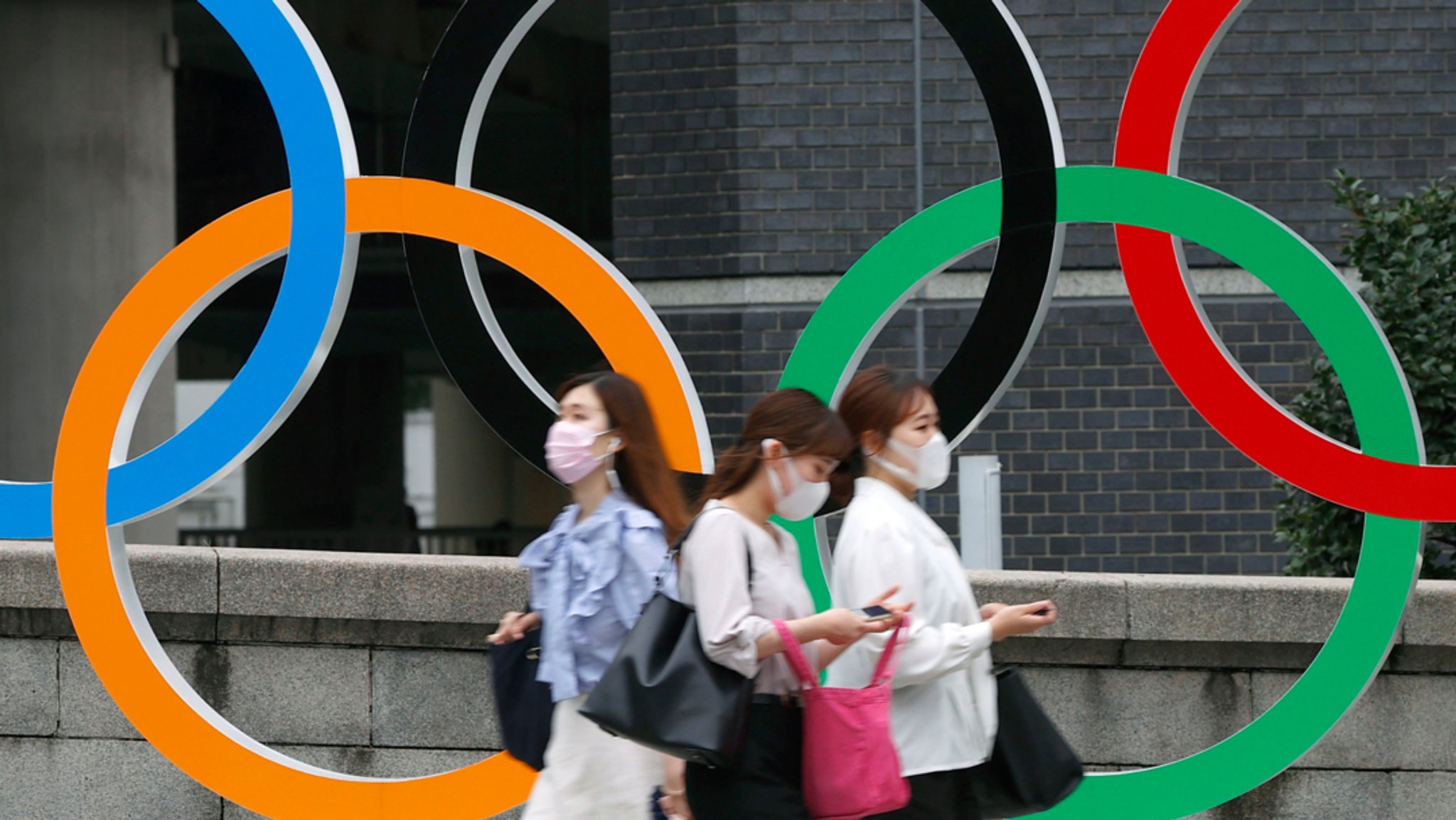 Japan, Tokio: Menschen mit Gesichtsmasken gehen an der Statue der Olympischen Ringe in Tokio vorbei.