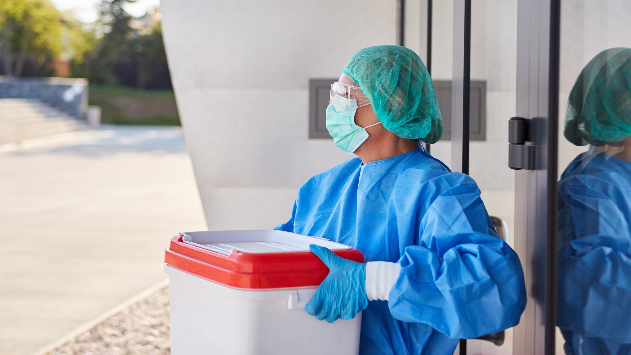 Symbolbild: Arzt oder Chirurg mit Organtransport nach Organspende für Operation vor Klinik Eingang in Schutzkleidung.