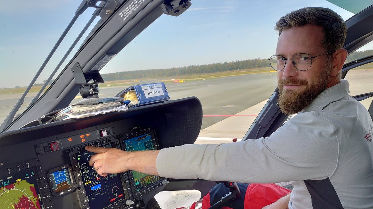 Pilot Stefan Schwabbauer sitzt im Cockpit und zeigt auf die digitalen Anzeigen. 