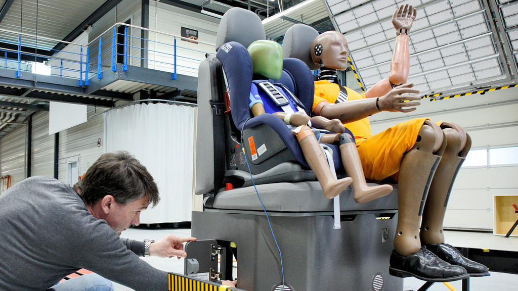 Zwei Crashtest-Dummys sitzen auf einer Autobank.