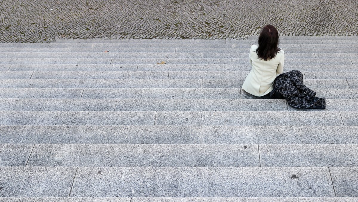 Eine Frau sitzt alleine auf einer weitläufigen Treppe