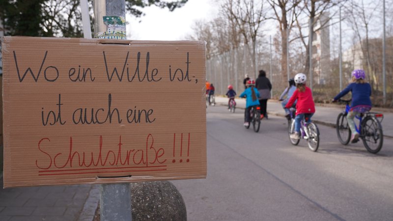 Schild "Wo ein Wille ist, ist auch eine Schulstraße" vor radelnden Menschen | Bild: Minh Duc Truong, ADFC Garching Schild "Wo ein Wille ist, ist auch eine Schulstraße" vor radelnden Menschen