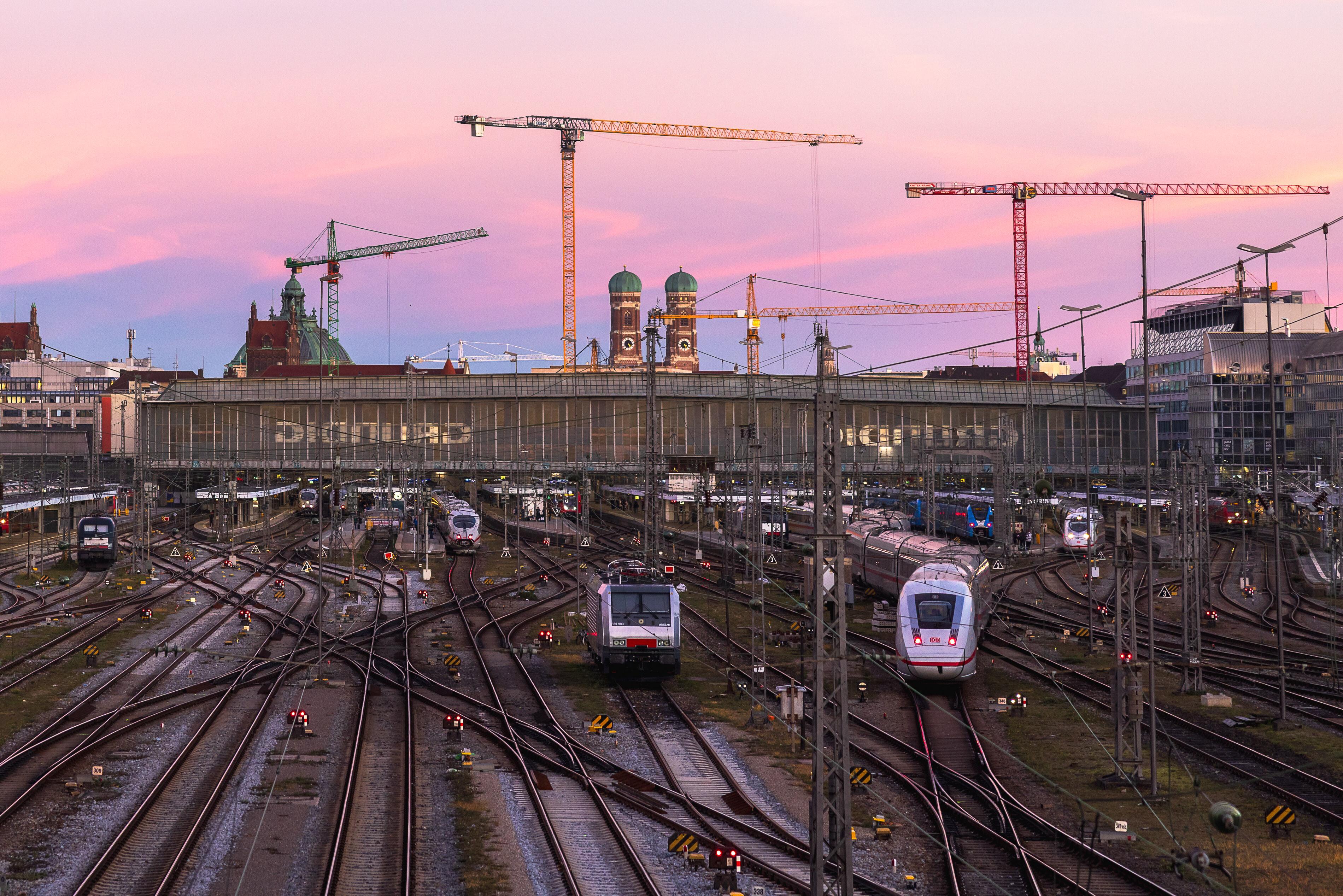 Blick auf die Gleisanlagen des Muenchner Hauptbahnhofs mit mehreren ein- und ausfahrenden Zuegen bei Abendlicht.