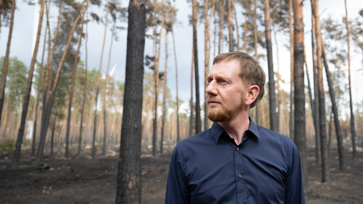 Michael Kretschmer (CDU), Ministerpräsident von Sachsen, begutachtet die Schäden in einem an Brandenburg angrenzenden Waldbrandgebiet. 