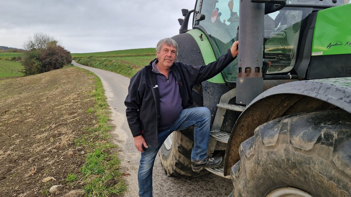 Neben einem grünen Traktor steht Landwirt Hans Steiner auf einer Straße am Feldrand.
