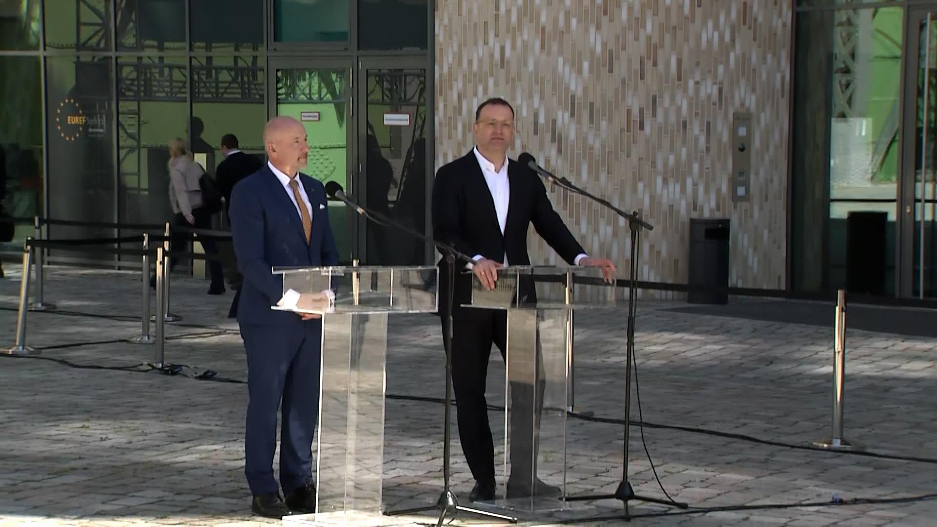 Zwei Männer im Anzug stehen bei einer Pressekonferenz im Freien an Rednerpulten.