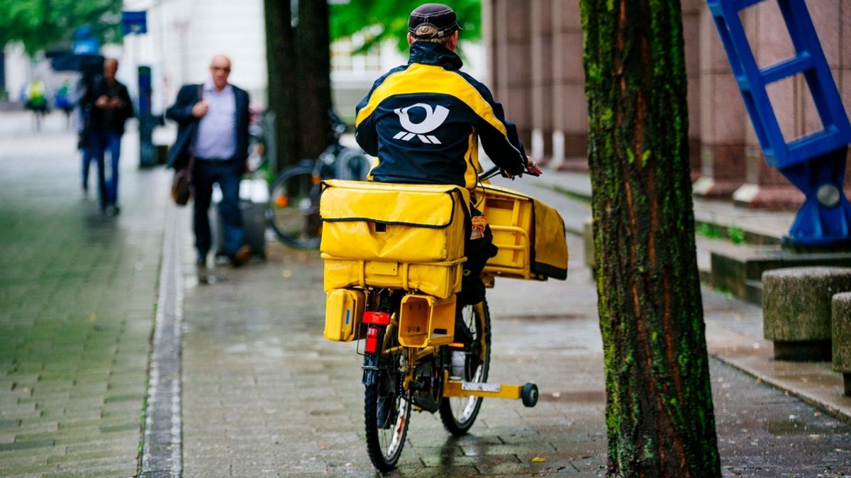 Ein schwer bepackter Postbote fährt mit dem Rad im Regen