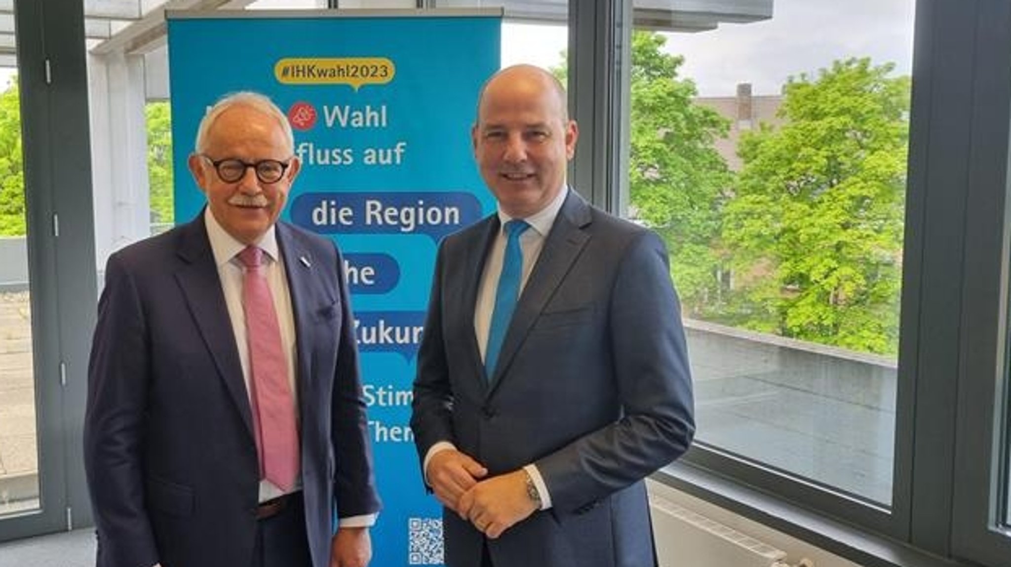 Zwei IHK-Funktionäre in AugsburgSchwabens IHK-Präsident Gerhard Pfeifer und Hauptgeschäftsführer Marc Lucassen stehen vor einem IHK-Plakat