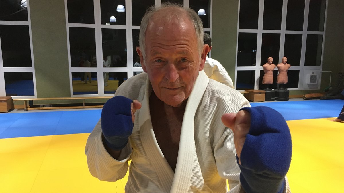 Ein älterer Mann in einer Sporthalle mit blauen Schutzhandschuhen.