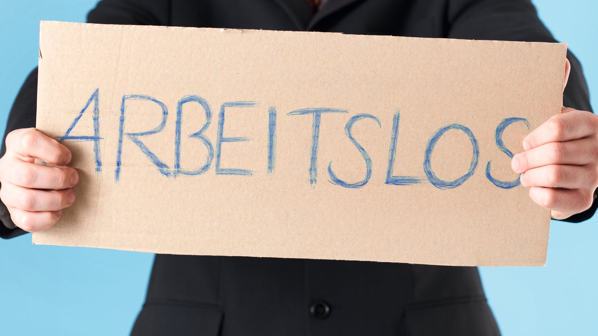 Mann hält Pappe mit der Aufschrift "Arbeitslos" in den Händen.