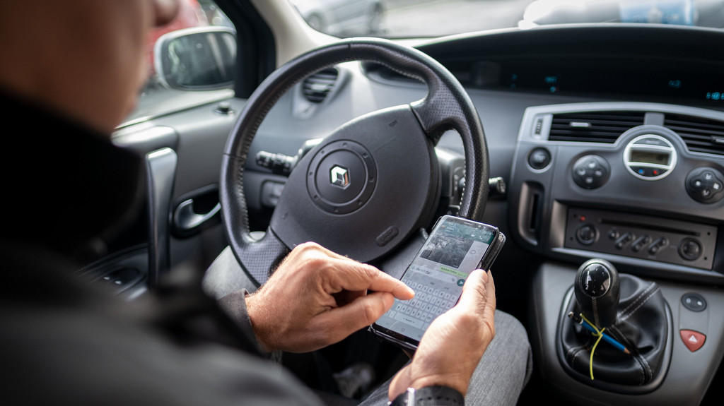 Ein Mann schreibt im Auto auf einem Smartphone eine Nachricht. 