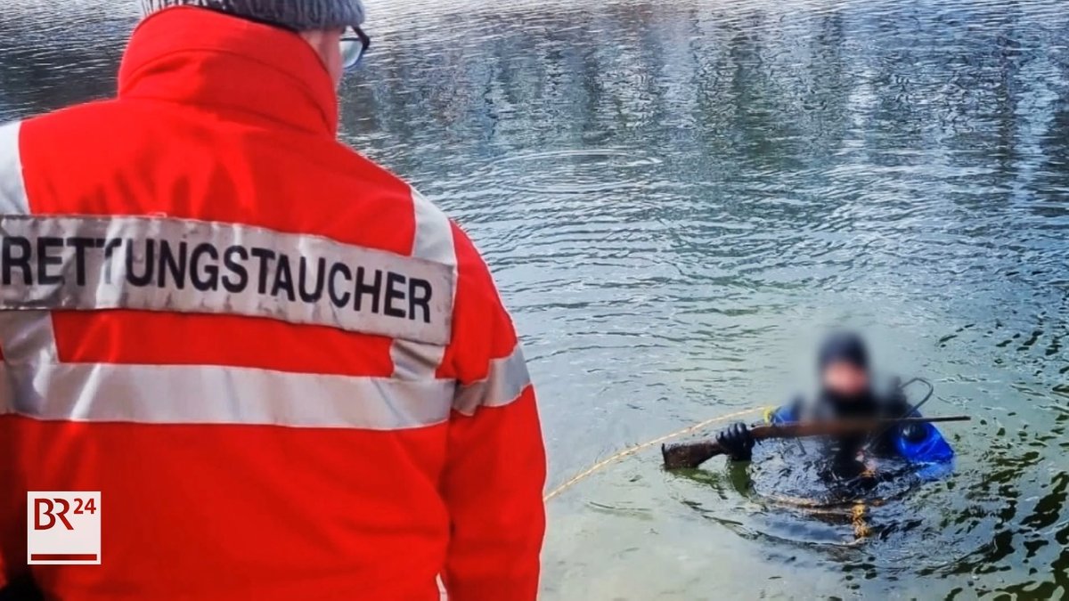 Ein Rettungstaucher taucht mit einer Waffe aus dem Wasser auf.
