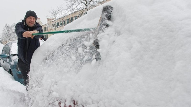 Mann fegt sein Auto von Schnee frei