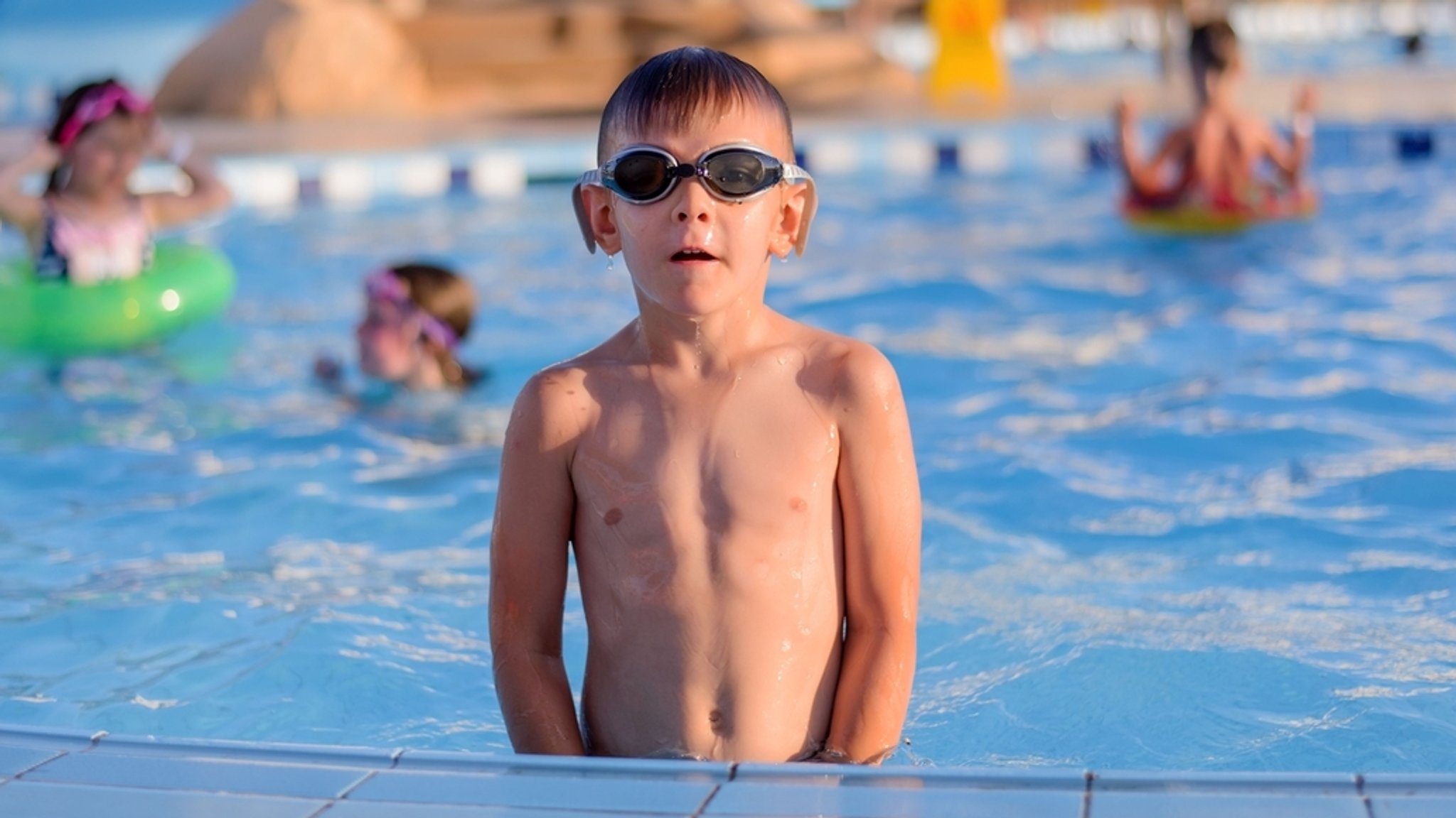 Ein Junge steht im Freibad im Wasser.