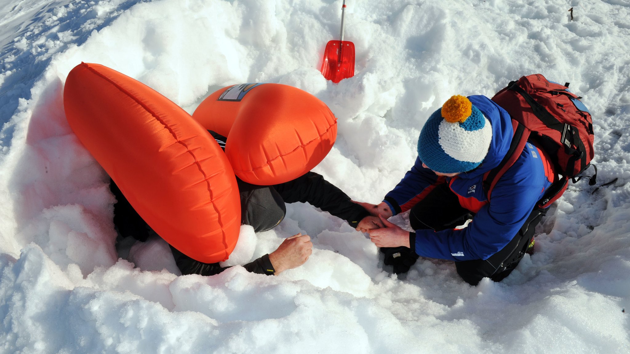 Mann mit Lawinenruckssack im Schnee mit Helfer.