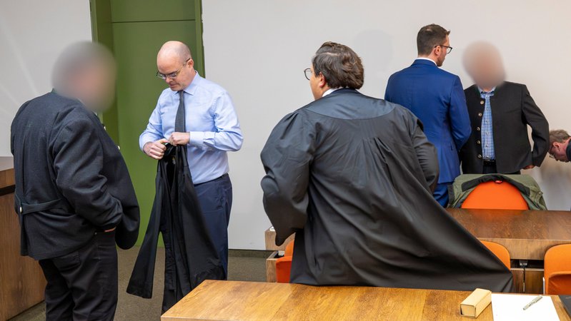 28.10.2025: Die zwei beschuldigten Bahnmitarbeiter (links und rechts) stehen vor Prozessbeginn um das tödliches Zugunglück in Garmisch-Partenkirchen vom 3. Juni 2022 mit ihren Anwälten zusammen im Gerichtssaal des Landgericht München II. | Bild: dpa-Bildfunk/Peter Kneffel 28.10.2025: Die zwei beschuldigten Bahnmitarbeiter (links und rechts) stehen vor Prozessbeginn um das tödliches Zugunglück in Garmisch-Partenkirchen vom 3. Juni 2022 mit ihren Anwälten zusammen im Gerichtssaal des Landgericht München II.