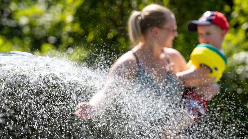 Eine Mutter mit Kind erfrischt sich an einem Wasserspiel im Sport- und Freizeitbad von der sommerlichen Hitze. | Bild: picture alliance/dpa | Michael Reichel Eine Mutter mit Kind erfrischt sich an einem Wasserspiel im Sport- und Freizeitbad von der sommerlichen Hitze.